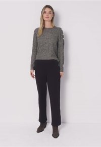 Szary sweter dzianinowy z okrągłym dekoltem i guzikami po bokach, w połączeniu z czarnymi, prostymi spodniami. Dopełnieniem stroju są buty w ciemnym odcieniu.