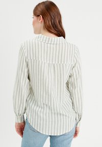 Chemise à manches longues rayée en crème et vert terne, avec un col, des poignets boutonnés et un hem arrondi.