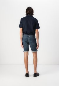 Chemise à manches courtes bleu marine foncé associée à un short en denim à revers. Des chaussures noires complètent la tenue. Présente une coupe décontractée et un design simple.