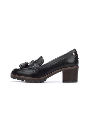 Mocasines de cuero negro con un taco bajo, borlas decorativas y una suela texturizada. Acabado suave con un detalle de costura clara en contraste.
