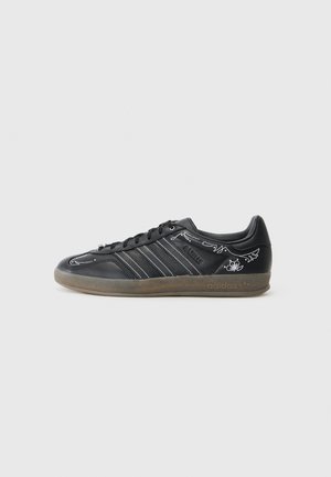 Baskets en cuir noir avec coutures blanches et détails graphiques en forme d'ailes. Dotées d'une semelle en caoutchouc et de trois rayures latérales. Branding Adidas présent.
