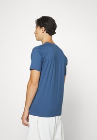 Blå bomulds t-shirt med korte ærmer, rund hals og en glat tekstur, set fra ryggen. Enkel design, ingen mønstre eller accenter.