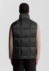Schwarze Steppweste mit hohem Kragen und gestepptem Design. Das Material wirkt glänzend und gepolstert, ohne sichtbare Hardware oder Akzente.