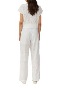 Weißes, gesticktes Zwei-Teile-Set bestehend aus einem kurzärmeligen Oberteil und weiten Hosen, mit floralen Ausschnittmustern und einer weichen Stofftextur.