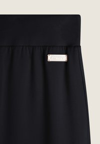 Tessuto elasticizzato nero con una cintura alta, caratterizzato da una targhetta lucida in oro rosa incisa con "FREDDY". Texture liscia, design semplice.