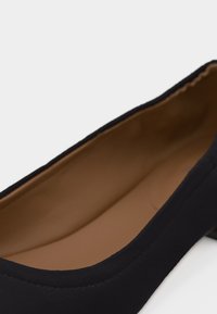 Μαύρο φλατ παπούτσι με στρογγυλεμένη μύτη και λεία ταμπά εσωτερική επένδυση, εμφανιζόμενο σε κοντινή λήψη.