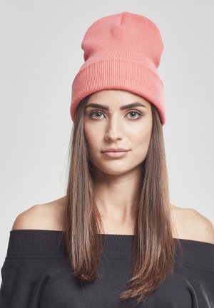 Korallfärgad stickad mössa med ribbat mönster, mjukt tyg och en lös passform, bärs tillsammans med en svart off-shoulder topp. Inga mönster eller detaljer synliga.