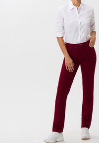 Pantalons en coton bordeaux au design ajusté, avec des poches avant et une taille avec passants de ceinture, associés à une chemise blanche à boutons et des baskets blanches.