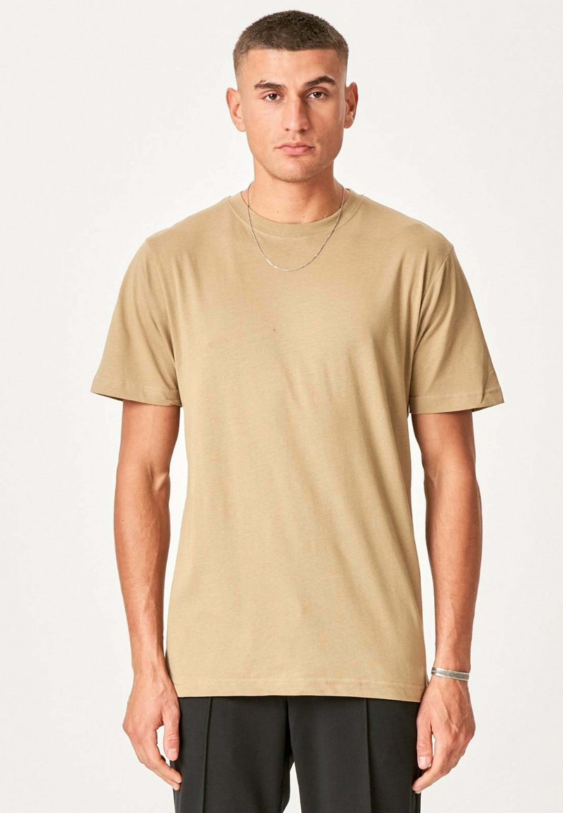 Beige bomulds t-shirt med rund halsudskæring og korte ærmer, der har en subtil tekstur og en afslappet pasform, båret med minimale accessories.