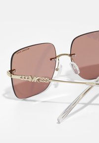 Óculos de sol retangulares com lentes rosadas, armação de metal dourado, apresentando um logotipo de elos na hastes e almofadas nasais transparentes.