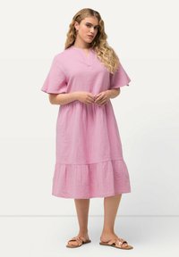 Rosa, kurzärmliges Kleid mit gestuftem Saum, strukturierter Stoff und V-Ausschnitt. Braune Sandalen mit einem Riemendesign und leichtem Absatz.