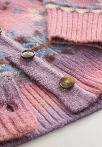 Neulejakku vaaleanpunaisissa ja violetissa sävyissä, varustettuna ribbireunoilla, kahdella ruskealla napilla ja pehmeällä, tekstuuripinnalla, jossa on kuviopainatus.