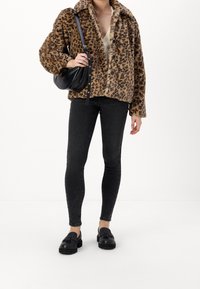 Giacca in pelliccia sintetica leopardata con collare oversize, abbinata a jeans skinny scuri e scarpe senza lacci nere. Borsa a spalla nera sul lato sinistro.