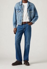 Chaqueta de denim azul claro con bolsillos laterales, camiseta blanca, jeans azul oscuro, cinturón marrón y zapatos marrón oscuro. Conjunto casual con un diseño clásico.