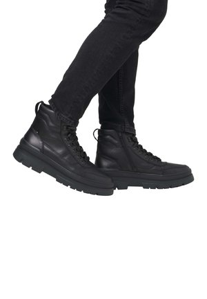 Botas negras de cuero hasta el tobillo con un acabado texturizado, cuello acolchado, parte delantera con cordones y suela de goma gruesa. Cierre lateral con cremallera para un acceso fácil.
