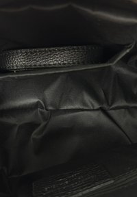 Wnętrze czarnej torby, na którym widoczny jest teksturowany czarny skórzany pasek na tle gładkiej czarnej podszewek.