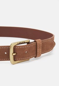 Rudas zomšinis diržas su žalvariniu užsegimu, ant kurio išgraviruotas "Levi's" logotipas. Siūtos kraštinės ir perforacijos dydžio reguliavimui.