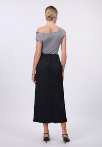 Gray off-the-shoulder top paired with a black pleated maxi skirt, featuring a textured fabric and a cinched waist detail.