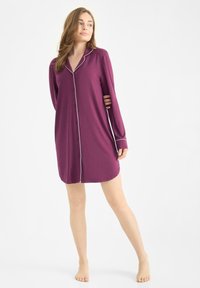 Vestido de pijama de manga larga en púrpura profundo con ribetes blancos, que presenta un cierre delantero de botones y un dobladillo ligeramente curvado. Textura de tela suave.