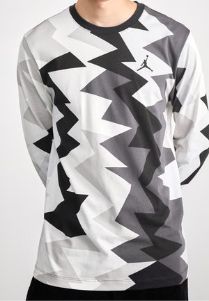 Mężczyzna w koszuli z długim rękawem w czarno-białym szarym wzór zygzakowym oraz małym logo Jumpman na górnej części klatki piersiowej.