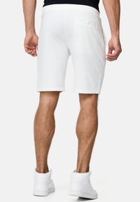 Hvide bomuldsshorts med lige snit, elastisk talje og en enkelt knaplukket baglomme, parret med hvide høj-top sneakers.