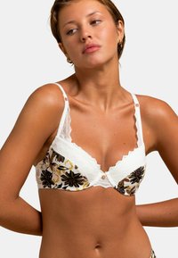 Soutien-gorge avec bordure en dentelle blanche, motif floral en noir, jaune et vert. Présente un design festonné et un détail de bouton au centre.