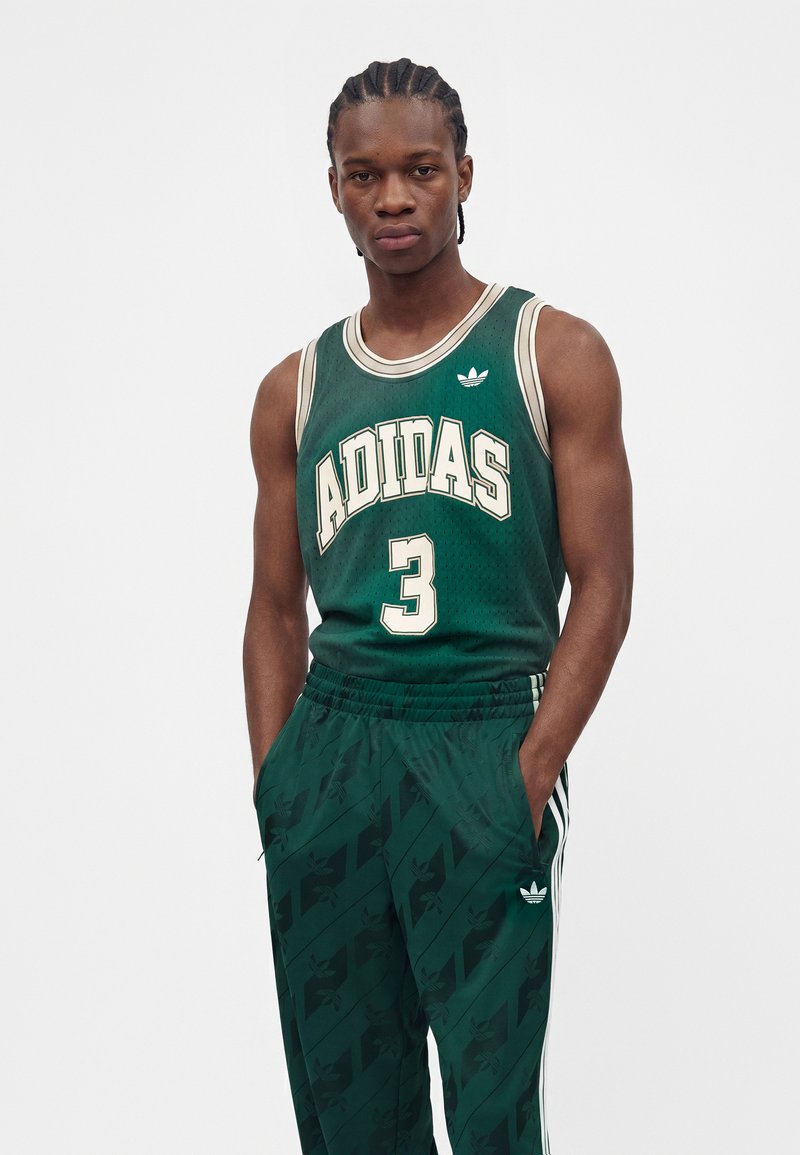 Junger Mann mit geflochtenem Haar trägt ein grünes Adidas Basketballtrikot mit der Nummer 3 und passende grüne Adidas-Hosen mit weißen Streifen.