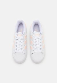 Vita atletiska skor med en texturerad gummitå, tre rosa ränder och snörning. Dämpad insida för komfort.