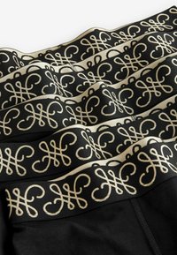 Tejido negro con una cinturilla decorativa que presenta intrincados patrones dorados. El diseño exhibe curvas y bucles, creando una apariencia texturizada.