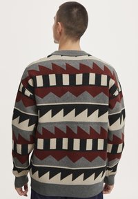 Knitted sweater in gray, burgundy, black, and ivory. Features geometric patterns with zigzag and stripe designs. Ribbed cuffs and hem.