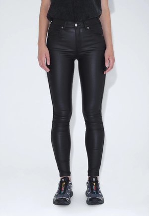 Black faux leather leggings with a smooth texture, high waist, and slim fit, paired with gray athletic shoes featuring colorful accents.