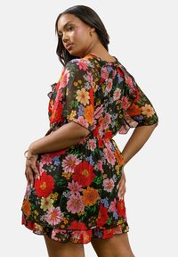 Kukallin mekko mustasta läpinäkyvästä kankaasta, kirkkaista monivärisistä kukista, lyhyillä hihoilla, elastisella vyötäröllä ja röyhelöhelmalla.