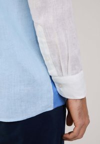 Camicia a maniche lunghe con corpo in lino azzurro chiaro, maniche in lino bianco e dettagli con polsini a bottoni. Tessuto morbido con un contrasto di colori a strati.