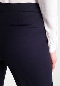 Kostymbyxor i marinblått med en texturerad tyg, med en slät bakficka och en mjuk midja, kombinerat med en vit långärmad skjorta.