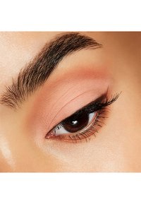 Närbild av ett öga med mjuk persikofärgad ögonskugga, väldefinierade ögonfransar, en mörk eyeliner och en slät hudtextur runt ögonområdet.