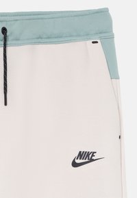 Šviesiai smėlio spalvos sportiniai šortai su mėlynu diržu, raišteliu ir juodu Nike logotipu ant kairiojo kojos. Pagaminti iš minkštos medvilnės mišinio audinio.