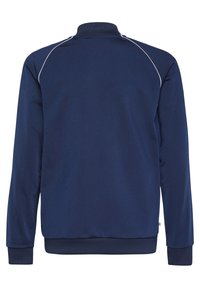 Námořnicky modrá sportovní bunda s dlouhými rukávy, vysokým límcem a bílým kontrastním prošíváním podél ramen. Hladká textura a žebrované manžety.