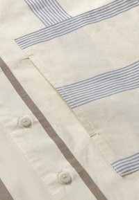 Leichtes Baumwollhemd aus kremfarbenem Stoff mit feinen blauen und braunen Streifen, einer Brusttasche und weißen Knopfverschlüssen.