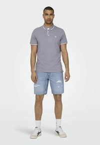 Heren grijze poloshirt met witte afwerking, gecombineerd met gescheurde denim shorts, witte sokken en witte sneakers. Eenvoudig ontwerp, casual pasvorm.