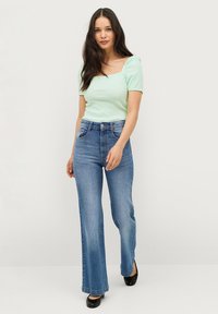 Muntgroene ribbel top met korte mouwen en lichtblauwe high-waisted flared jeans. De outfit heeft een vierkante halslijn en een aansluitende silhout.