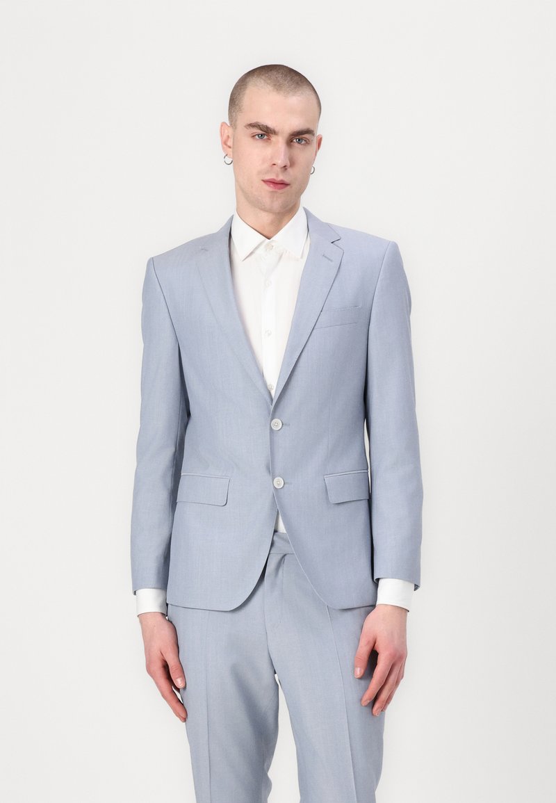Costum bleu deschis cu un design ajustat, prezentând o jachetă cu un singur rând de nasturi, două nasturi și rever cu tăietură; purtat peste o cămașă albă.