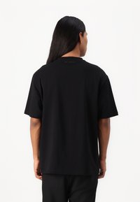 Μαύρη κοντομάνικη μπλούζα φτιαγμένη από μαλακό ύφασμα, με έναν απλό σχεδιασμό, στρογγυλή λαιμόκοψη και διακριτική επωνυμία στο πίσω μέρος.