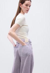 Ελαφρώς μπεζ ριγωτό τοπ με κοντά μανίκια, συνδυασμένο με ψηλόμεσα μωβ τζιν παντελόνια που έχουν ταμπελάκι με λογότυπο και λεπτομέρειες πίσω στην τσέπη.