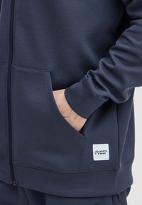 Marineblauwe rits hoodie met een gladde structuur, voorzakken en een genaaid wit label met de tekst "NORTH BEND" op de linkeronderzijde.