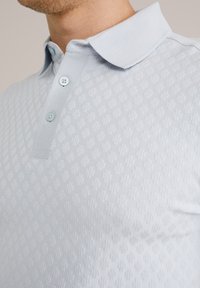Camisa polo azul claro con un patrón texturizado, un cuello clásico y tres botones en el escote. Acabado de tela suave.