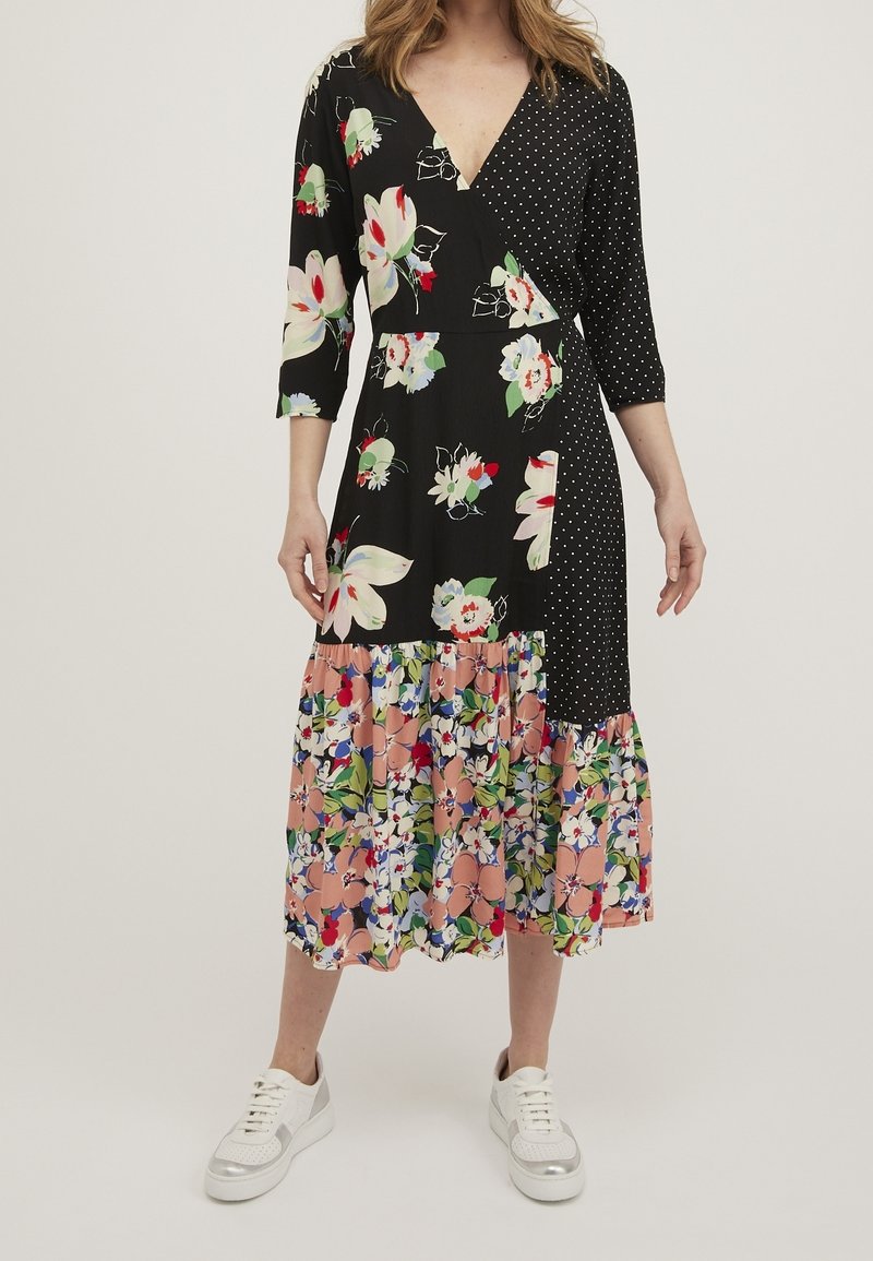 Musta kietaisumekko, jossa on kukkakuosisia ja pilkullisia yksityiskohtia, ¾-hihat ja kerroksellinen, värikäs kukkainen hame. Yhdistetty valkoisiin lenkkareihin.