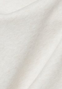 Baumwollstoff in einer cremigen, off-weißen Farbe mit einer weichen, glatten Textur und subtilen Lichtvariationen, die in sanften Falten fällt.