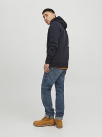 Felpa navy con tasca a marsupio, jeans in denim blu e stivali in camoscio beige. Cuffs arrotolati visibili sui jeans e dettagli cuciti sugli stivali.