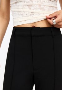 Pantalons noirs sur mesure avec une texture lisse, dotés d'une taille avec passants de ceinture et d'un design avant épuré, associés à un haut en dentelle léger.
