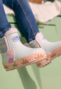Bottes de pluie en caoutchouc bleu clair avec des accents roses, ornées d'un motif Peppa Pig et d'un motif ludique d'éclaboussures de boue sur la semelle.